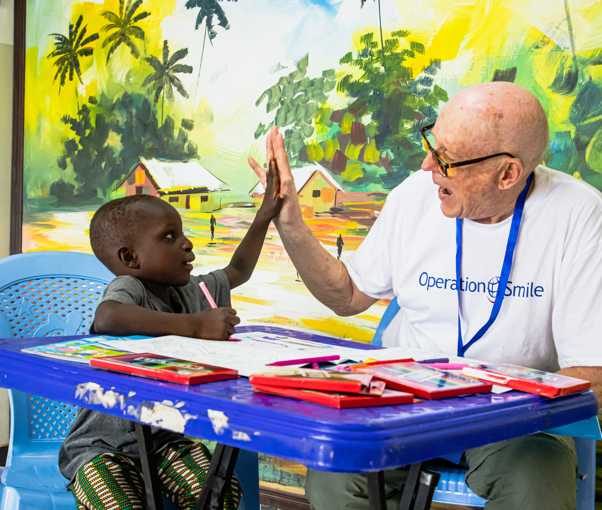 En man med glasögon sitter vid ett bord och gör high five med en liten pojke.